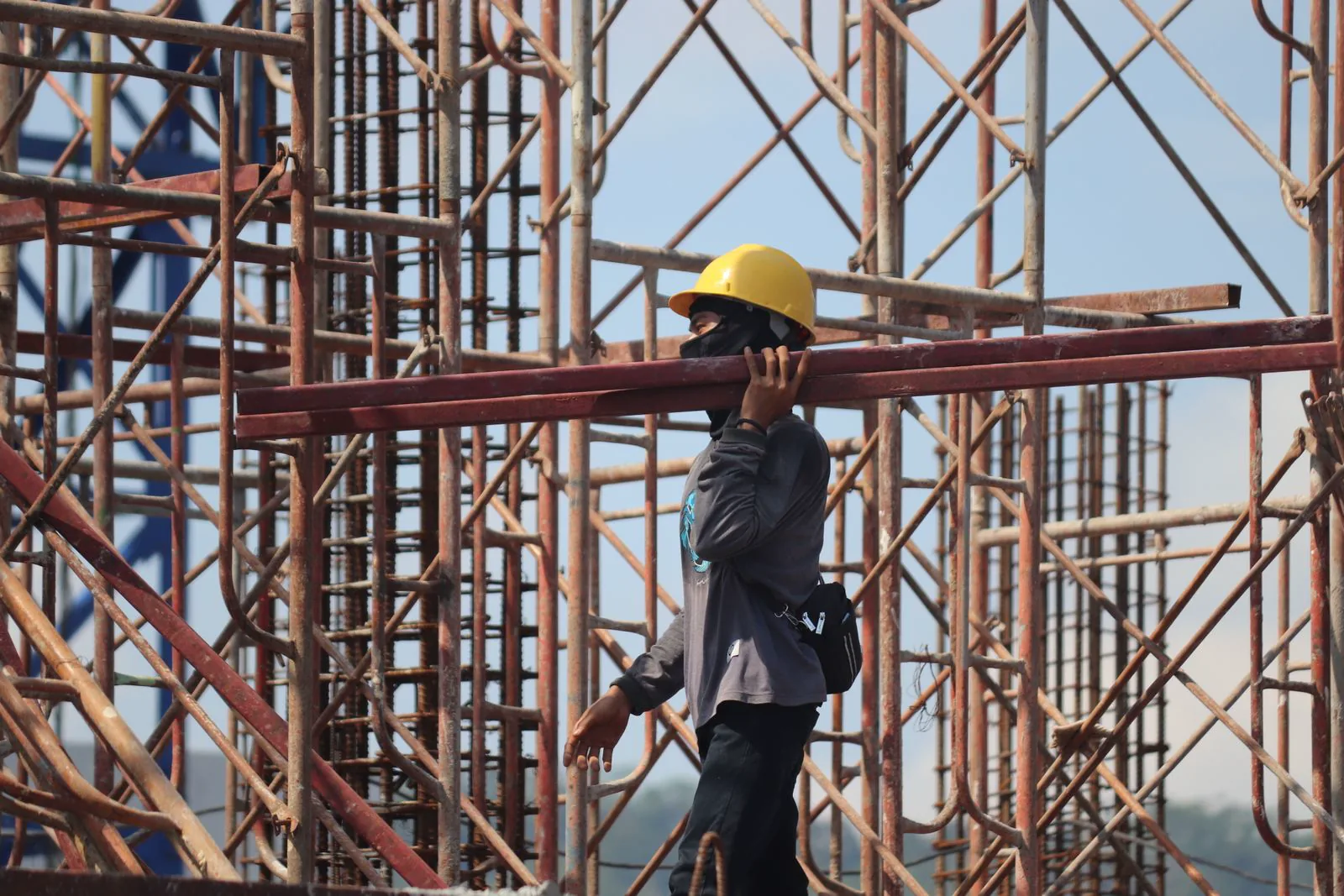 A worker in a hard hat carrying reinforcing steel on a construction site.